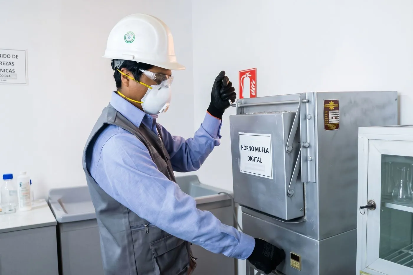 Técnico con equipo de protección operando el horno mufla digital del laboratorio químico